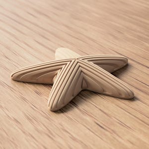 May include: A light-colored wooden starfish with detailed grooves, resting on a wooden surface. The starfish is a decorative item, possibly for coastal or nautical-themed decor.