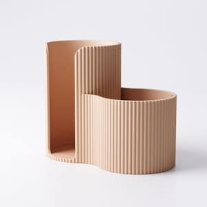 May include: A beige, two-part desk organizer with a ribbed texture. The organizer has a tall, curved section and a shorter, wider section, both connected and open at the top. The design is minimalist and modern.