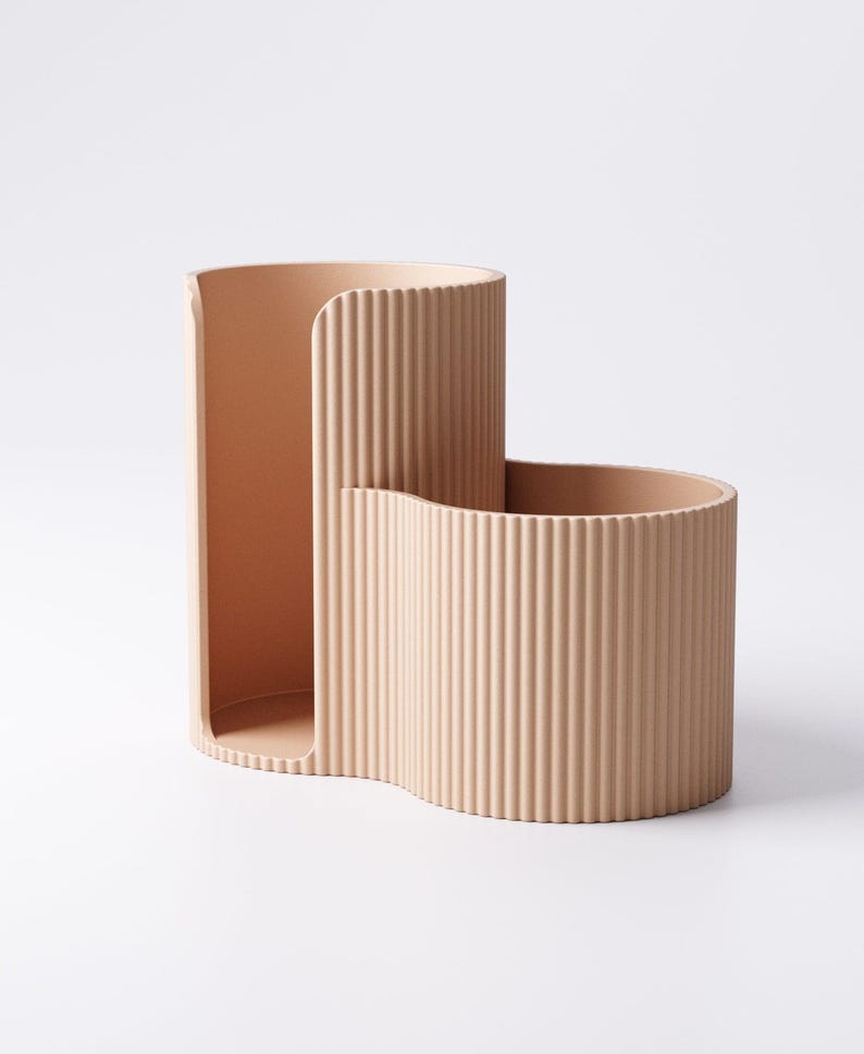 May include: A beige, two-part desk organizer with a ribbed texture. The organizer has a tall, curved section and a shorter, wider section, both connected and open at the top. The design is minimalist and modern.