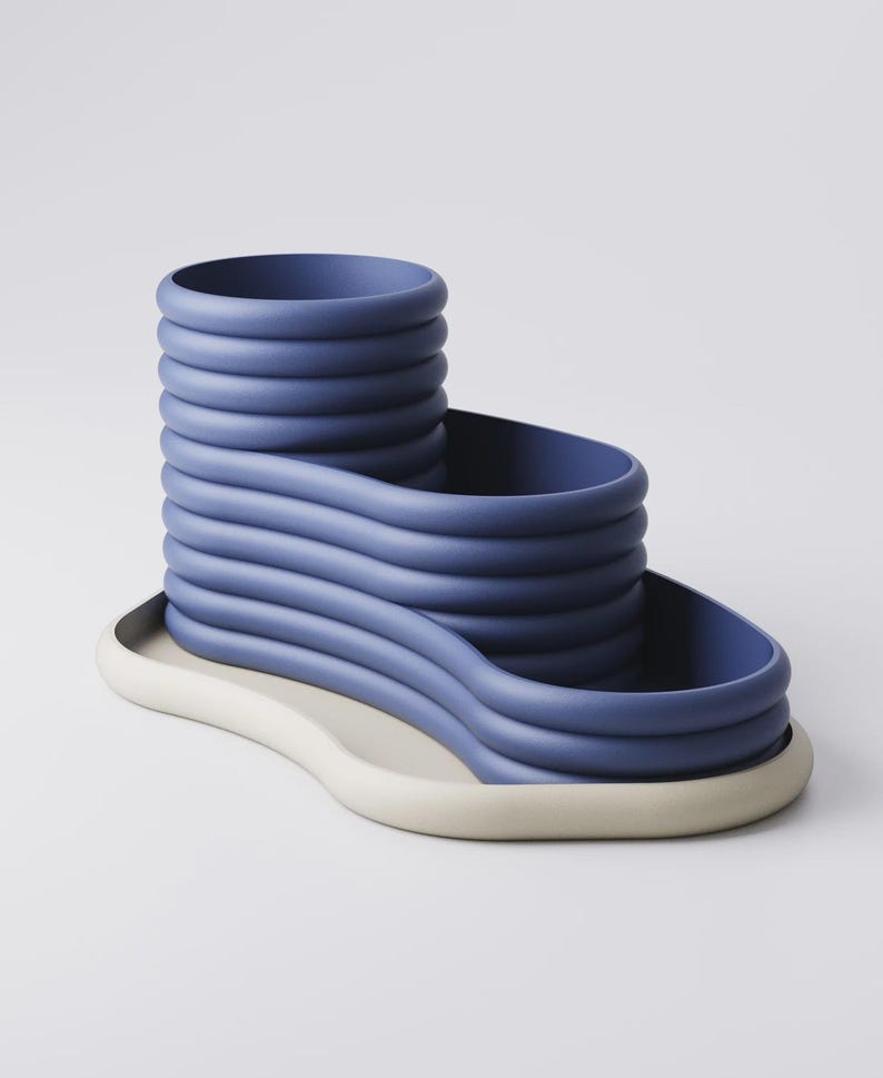 May include: A modern, abstract sculpture in shades of blue and off-white. The blue portion features a stacked, wavy design, while the base is a contrasting off-white, creating a unique, artistic piece. The sculpture is likely ceramic or a similar material.