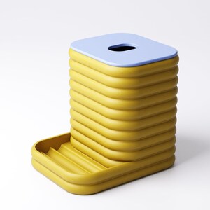 May include: A yellow and blue tissue box with a unique, ribbed design. The tissue box has a rectangular shape with a light blue top and a small opening. A small tray is attached to the side.