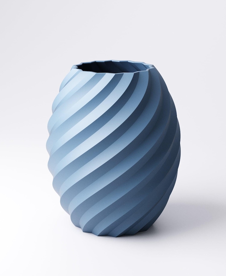 May include: A blue vase with a spiral design. The vase has a textured surface and a wide opening. The color of the vase is a gradient of blue shades, creating a modern and stylish look. The vase is suitable for home decor.