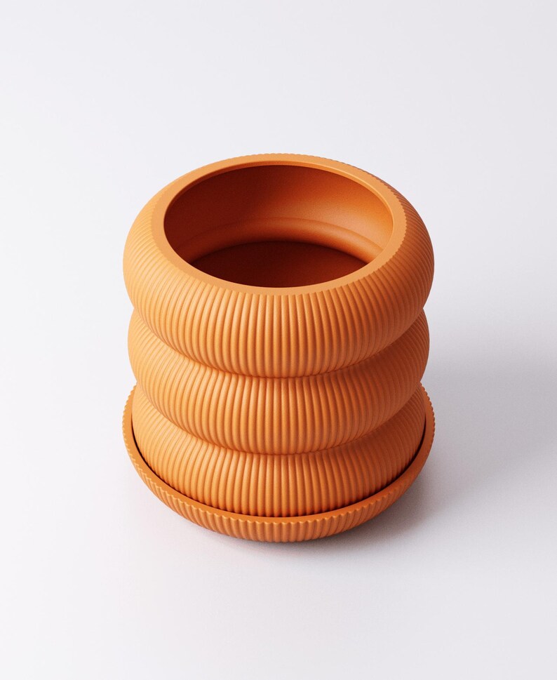 May include: A terracotta-coloured, ribbed plant pot with a matching saucer. The pot features a distinctive design with three stacked, rounded sections. The textured surface and warm colour create a modern aesthetic, suitable for indoor plants.