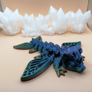 May include: A detailed, multi-colored dragon figurine with intricate wing designs and a textured body. The dragon is primarily blue with hints of green and purple. In the background are several white crystal formations.