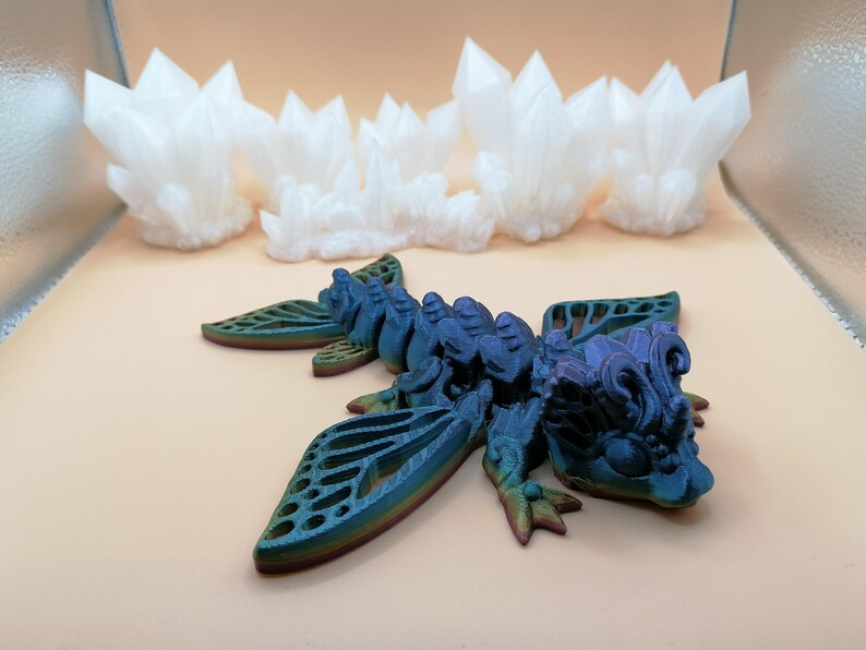 May include: A detailed, multi-colored dragon figurine with intricate wing designs and a textured body. The dragon is primarily blue with hints of green and purple. In the background are several white crystal formations.