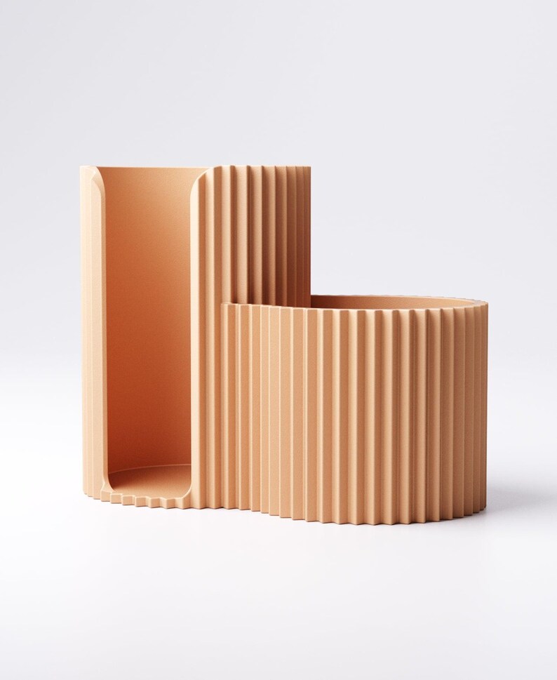 May include: A peach-colored, modern desk organizer with a unique, curved design. The organizer features a tall, rectangular section and a shorter, rounded section, both with vertical ridged detailing. The open design allows for easy access to stored items.