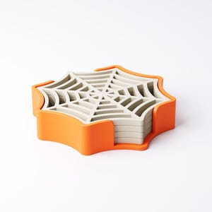 May include: A set of spiderweb-shaped coasters in a bright orange holder. The coasters are light gray and stack neatly. The holder has a curved design. A fun and functional item for Halloween or spooky decor.