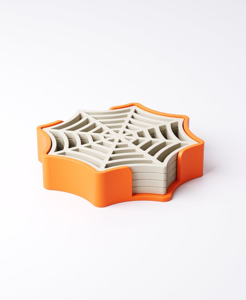 May include: A set of spiderweb-shaped coasters in a bright orange holder. The coasters are light gray and stack neatly. The holder has a curved design. A fun and functional item for Halloween or spooky decor.