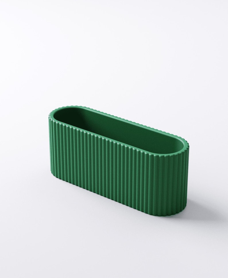 May include: A green, oval-shaped planter with vertical ribbed detailing. The planter has a smooth interior and a textured exterior. The design is modern and minimalist, suitable for various plants and decor styles.
