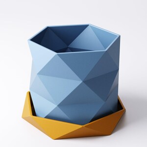 May include: A geometric, blue planter with a matching yellow base. The planter has a faceted design, creating a modern and stylish look. The planter is designed to hold plants and flowers. The planter is made of a durable material.