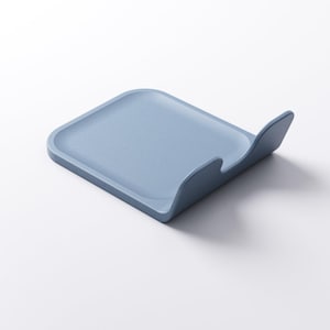 Op de afbeelding: Een lichtblauwe, vierkante lepelhouder met een gebogen rand. Gemaakt van een stevig materiaal en staat op een witte ondergrond. Het ontwerp is eenvoudig en modern, geschikt voor gebruik in de keuken. Afmetingen in centimeters.