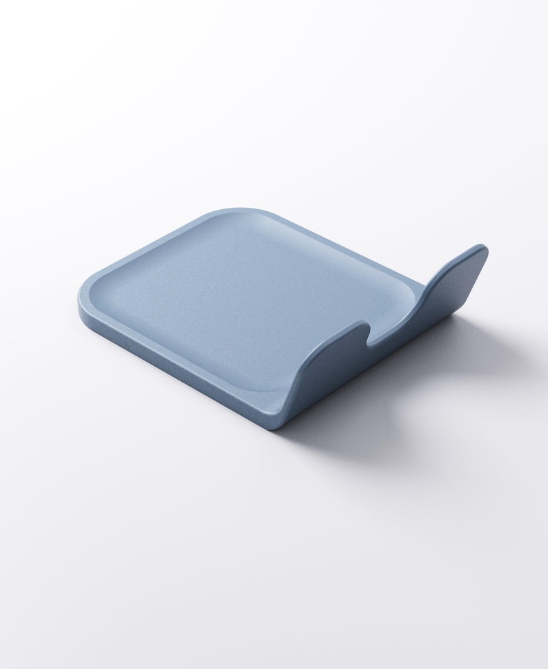 Op de afbeelding: Een lichtblauwe, vierkante lepelhouder met een gebogen rand. Gemaakt van een stevig materiaal en staat op een witte ondergrond. Het ontwerp is eenvoudig en modern, geschikt voor gebruik in de keuken. Afmetingen in centimeters.
