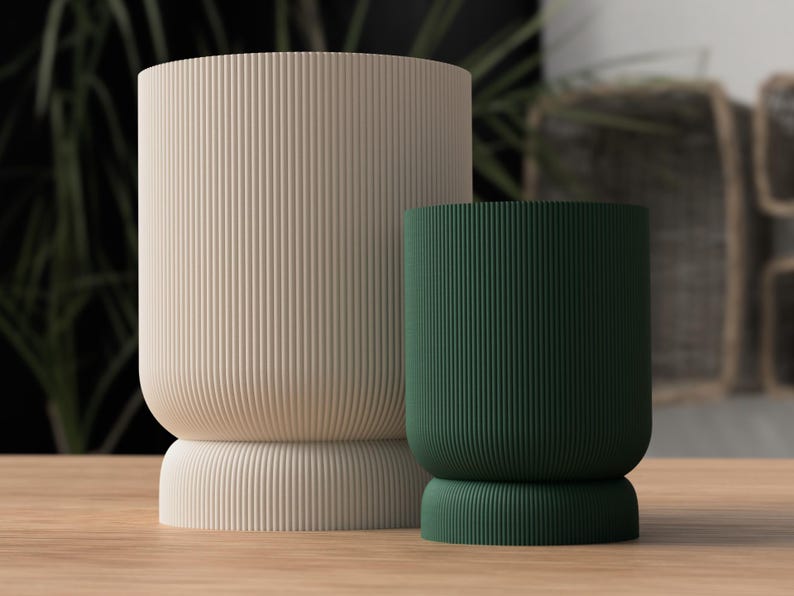 May include: Two cylindrical vases with vertical ribbed texture. One is a light beige color, and the other is a deep green. Both have a rounded base and a wider, rounded top. The vases are displayed on a wooden surface.