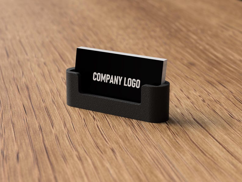 May include: A black business card holder with a black business card that reads "COMPANY LOGO" in white lettering. The holder is on a wooden surface.