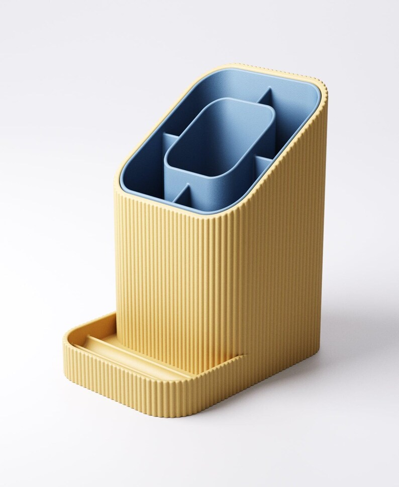May include: A yellow and blue desk organizer with a ribbed exterior. The organizer has a rectangular base with a small tray and an angled top. The interior features a blue compartment with several sections for storage.