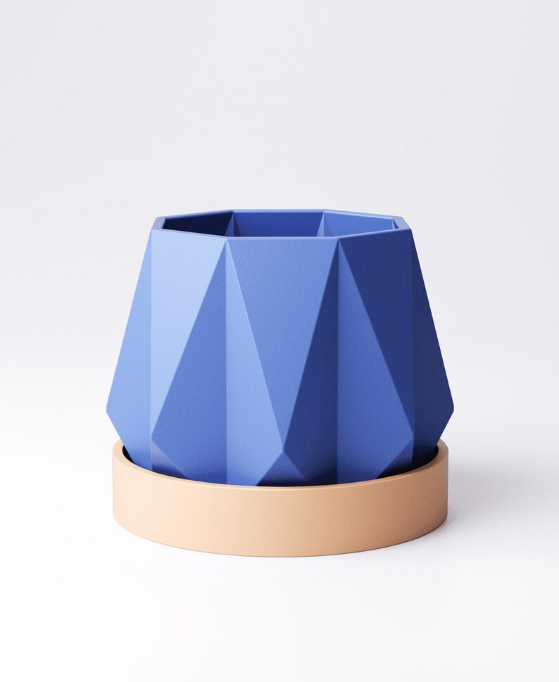 May include: A geometric, blue planter with a matching beige saucer. The planter has a faceted design and a hexagonal top. The saucer is a simple, rounded shape. The planter and saucer are made of a solid material.