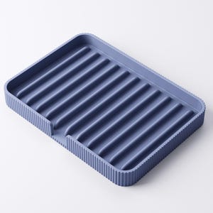 May include: A blue rectangular dish drying rack with a ribbed interior and a textured, ridged border. The rack has a small cutout on one side. The color is a muted, dusty blue.