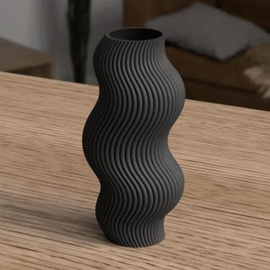 May include: A black, wavy-shaped vase with a textured, ridged surface. The vase has a narrow neck and a wider base, standing on a wooden surface. The design is modern and minimalist.