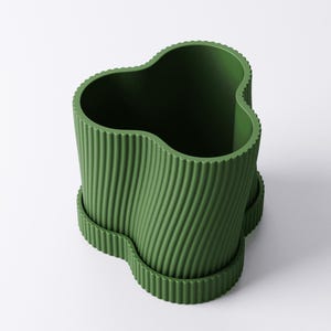 May include: A green, wavy-edged planter with a ribbed texture. The planter has a unique, organic shape and sits on a matching base. The design is modern and minimalist, suitable for indoor or outdoor use.