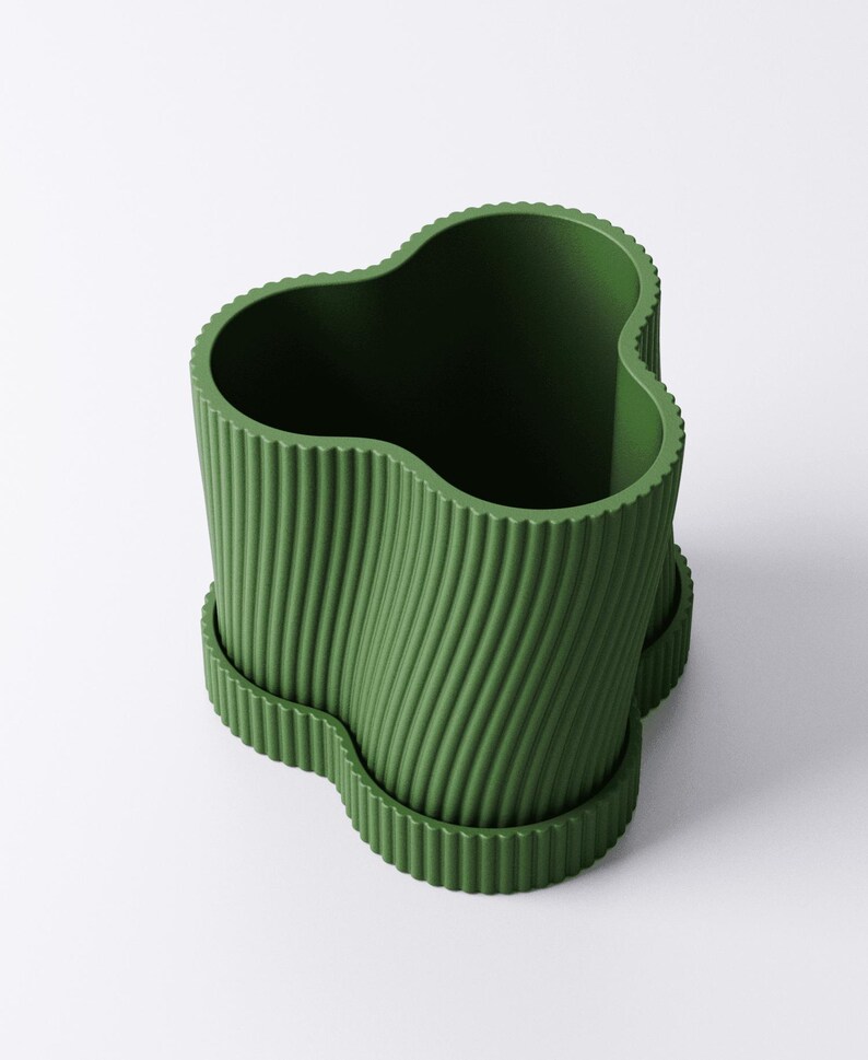 May include: A green, wavy-edged planter with a ribbed texture. The planter has a unique, organic shape and sits on a matching base. The design is modern and minimalist, suitable for indoor or outdoor use.
