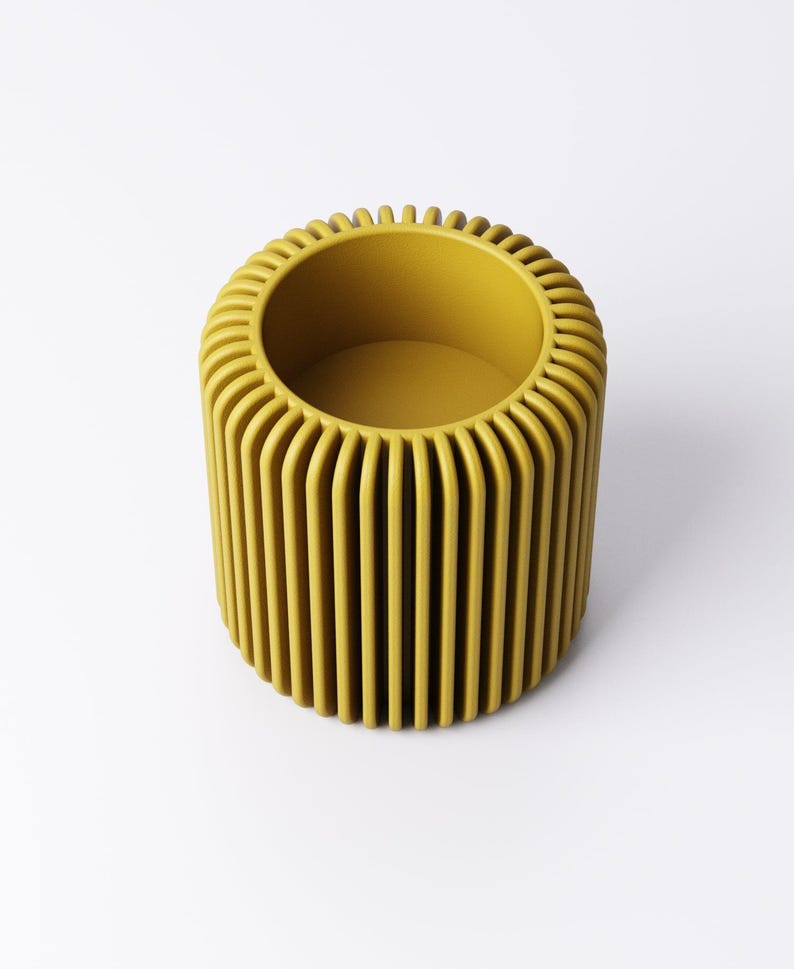 May include: A cylindrical, mustard-yellow decorative container with vertical, rounded ridges. The top edge has a series of small, vertical ridges. The interior is a matching mustard yellow. The container is set against a white background.