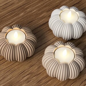 May include: Three decorative candle holders in the shape of flowers, each with a glowing LED candle. The holders are in shades of gray and beige, with a ribbed design. The candles emit a warm, inviting light.