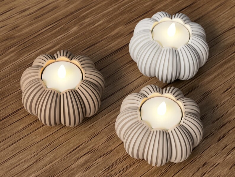 May include: Three decorative candle holders in the shape of flowers, each with a glowing LED candle. The holders are in shades of gray and beige, with a ribbed design. The candles emit a warm, inviting light.