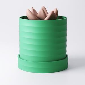 Op de afbeelding: Een groene, cilindrische plantenbak met horizontale ribbels, met een lichtbruine vetplant. De plantenbak staat op een bijpassende schotel. Het ontwerp is modern en minimalistisch.