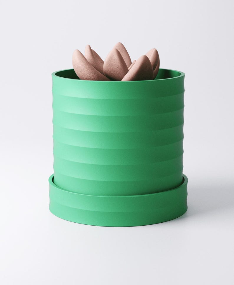 Op de afbeelding: Een groene, cilindrische plantenbak met horizontale ribbels, met een lichtbruine vetplant. De plantenbak staat op een bijpassende schotel. Het ontwerp is modern en minimalistisch.