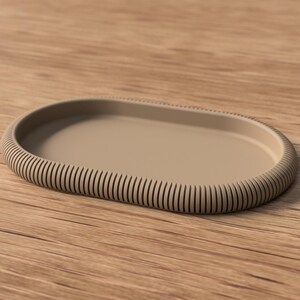 Puede incluir: Una bandeja ovalada beige con borde acanalado. La bandeja tiene un interior liso y plano y un borde elevado y texturizado. El borde acanalado a&ntilde;ade un elemento decorativo al dise&ntilde;o de la bandeja. La bandeja es de material s&oacute;lido.