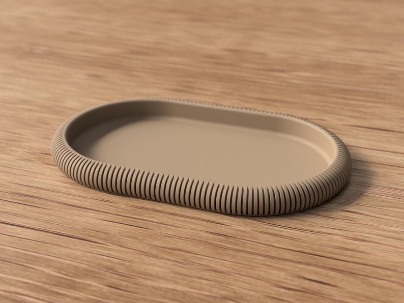 Puede incluir: Una bandeja ovalada beige con borde acanalado. La bandeja tiene un interior liso y plano y un borde elevado y texturizado. El borde acanalado a&ntilde;ade un elemento decorativo al dise&ntilde;o de la bandeja. La bandeja es de material s&oacute;lido.