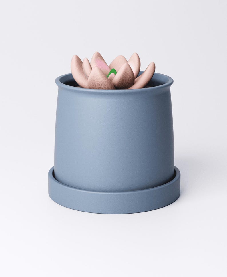May include: A blue ceramic planter with a matching saucer holds a faux succulent. The succulent features soft pink petals with green accents. The planter has a simple, modern design, suitable for home decor.