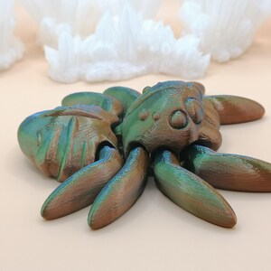 Op de afbeelding: Een 3D-geprinte octopussculptuur met een getextureerd oppervlak en iriserende kleuren. De sculptuur heeft een mix van groen, blauw en brons. De octopus heeft acht tentakels en een gedetailleerde kop. De achtergrond bevat witte, kristallijne formaties.