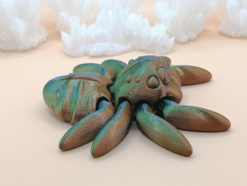 Op de afbeelding: Een 3D-geprinte octopussculptuur met een getextureerd oppervlak en iriserende kleuren. De sculptuur heeft een mix van groen, blauw en brons. De octopus heeft acht tentakels en een gedetailleerde kop. De achtergrond bevat witte, kristallijne formaties.
