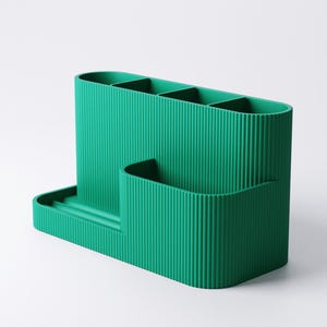 Pode incluir: Um organizador de secret&aacute;ria verde-azulado com textura canelada. Possui quatro compartimentos verticais, um pequeno bolso lateral e uma bandeja. O organizador &eacute; feito de um material s&oacute;lido e foi projetado para guardar canetas, l&aacute;pis e outros materiais de escrit&oacute;rio.