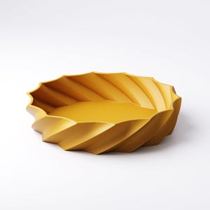 May include: A mustard-yellow decorative bowl with a unique, ridged design. The bowl has a shallow, oval shape with a textured exterior. The ridges create a spiral effect around the bowl's edge. The interior is smooth and the bowl is set against a white background.