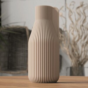 May include: A beige wooden vase with vertical brown stripes. The vase has a rounded base and a handle on the side. The vase is sitting on a wooden surface.