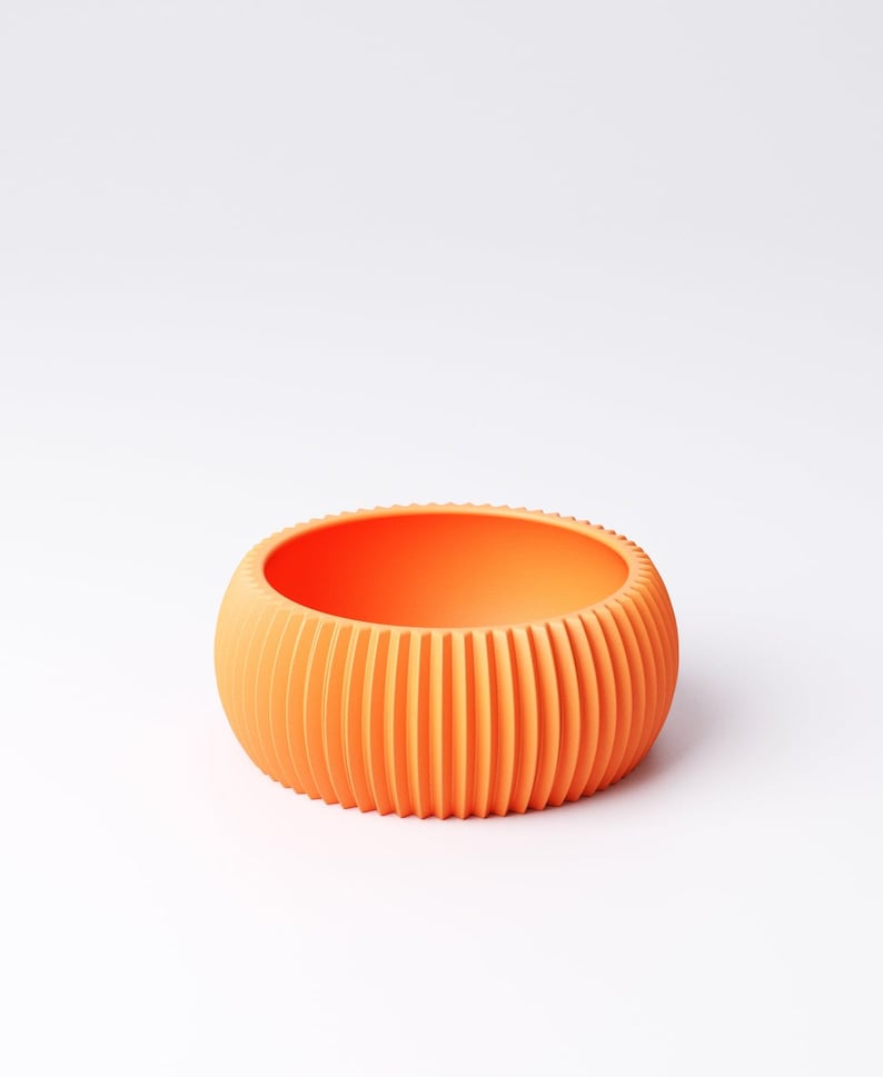 May include: An orange, round bowl with vertical ridged detailing. The bowl has a smooth interior and a textured exterior. The color is a vibrant, solid orange. The bowl is likely made of plastic or ceramic.