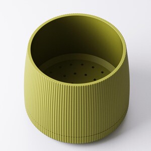 May include: A green, cylindrical container with a ridged exterior and a perforated interior base. The container has a wide opening and a slightly tapered shape, suitable for various uses. The color is a muted, olive green.