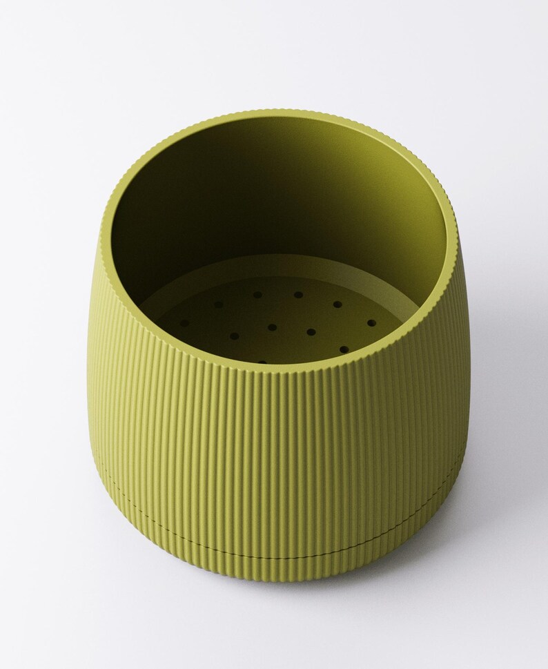 May include: A green, cylindrical container with a ridged exterior and a perforated interior base. The container has a wide opening and a slightly tapered shape, suitable for various uses. The color is a muted, olive green.