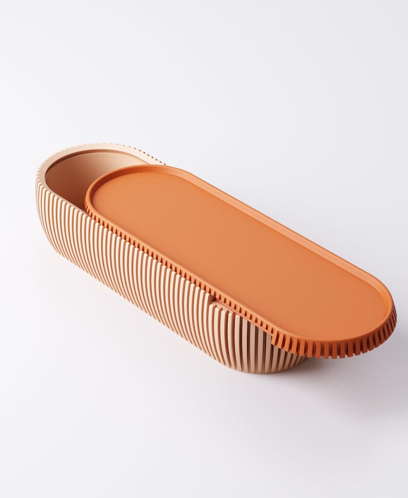 May include: An oval-shaped wooden storage box with a lid. The box is made of vertical wooden slats and has a light brown color. The lid is a solid orange color. The box is open, revealing the interior.