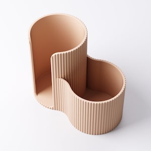 May include: A peach-colored desk organizer with a unique, wavy design. The organizer has three distinct sections: a tall, open compartment, a smaller, curved section, and a wider, open area. The exterior features vertical ribbed detailing.