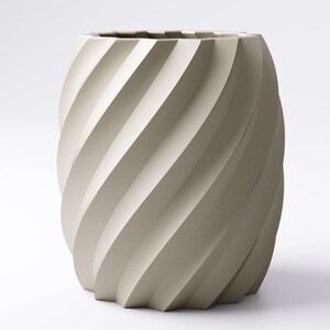 May include: A beige, cylindrical vase with a spiral design. The vase has a textured surface and a geometric base. The interior is dark, and the overall aesthetic is modern and minimalist. The vase is suitable for home decor.