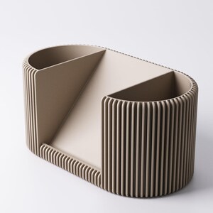 May include: A beige desk organiser with a distinctive design. It features two rounded compartments and a central section, all with vertical ribbed detailing. The oval shape and neutral colour make it suitable for any office or home decor.
