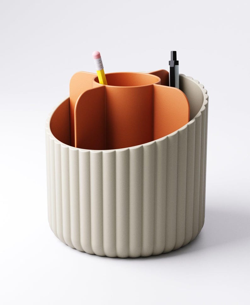 May include: A beige and orange desk organizer with a fluted exterior. The interior features a central orange compartment and several sections for pens and pencils. A yellow pencil and a black pen are visible.