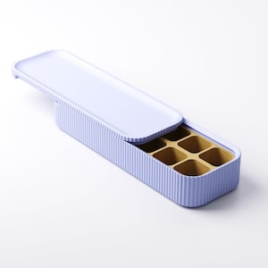 May include: A light purple ice cube tray with a matching lid. The tray has a ribbed exterior and contains six square compartments. The interior of the tray is a golden color.