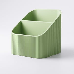 May include: A light green desk organizer with two compartments. The organizer has a ribbed texture on the exterior and a curved top. The item is designed to hold pens, pencils, or other office supplies.