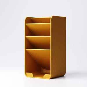 May include: Mustard yellow desk organizer with four angled compartments. The organizer has a rounded top and bottom with vertical ribbed detailing on the sides. The compartments are designed to hold papers or office supplies.