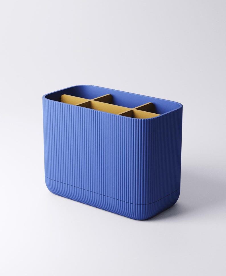 May include: A rectangular desk organizer with a vibrant blue exterior featuring a vertical ribbed texture. The interior is divided into six compartments by mustard yellow dividers, creating a structured space for holding various small items.
