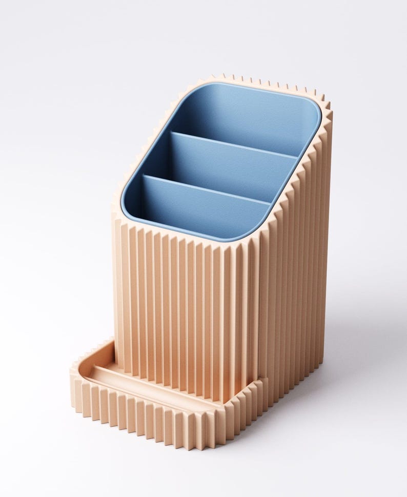 May include: A peach-colored desk organizer with a blue interior and three compartments. The organizer has a rectangular base with a small tray and a ridged exterior design. The interior is a light blue color.